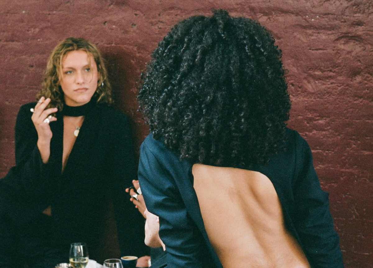 The backless blazer seen from behind, a figure smoking against a dark red wall