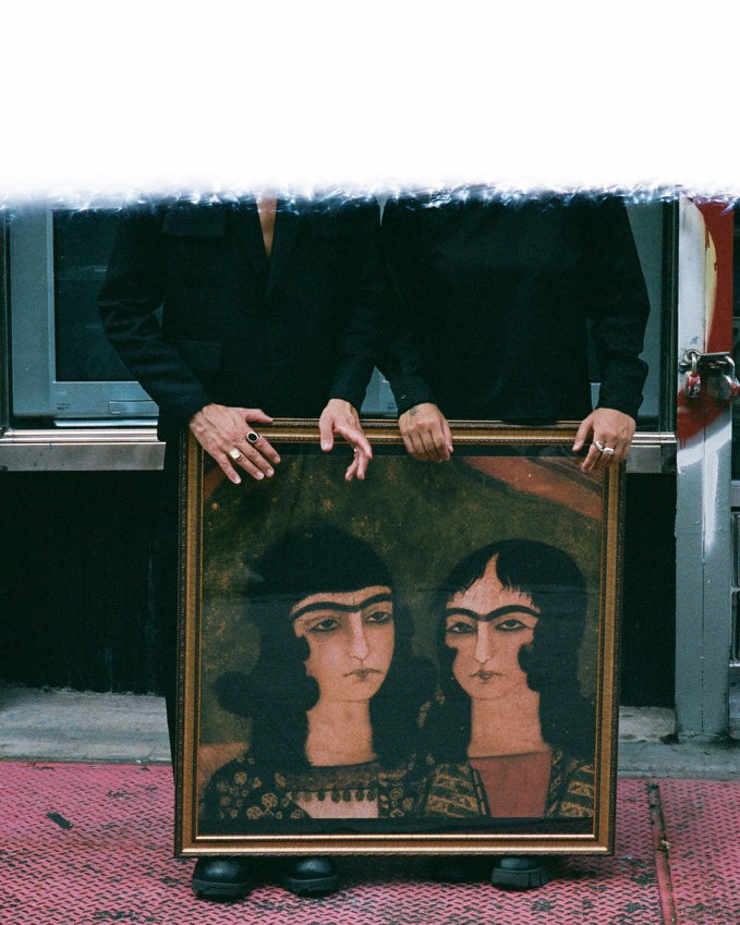 Two figures holding up a painting of two women on the sidewalk