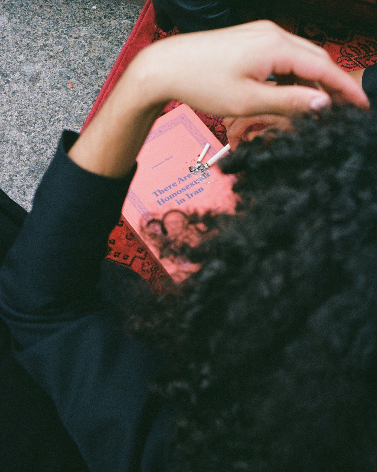 Overhead view of a figure with curly hair reading a pink book on a red rug