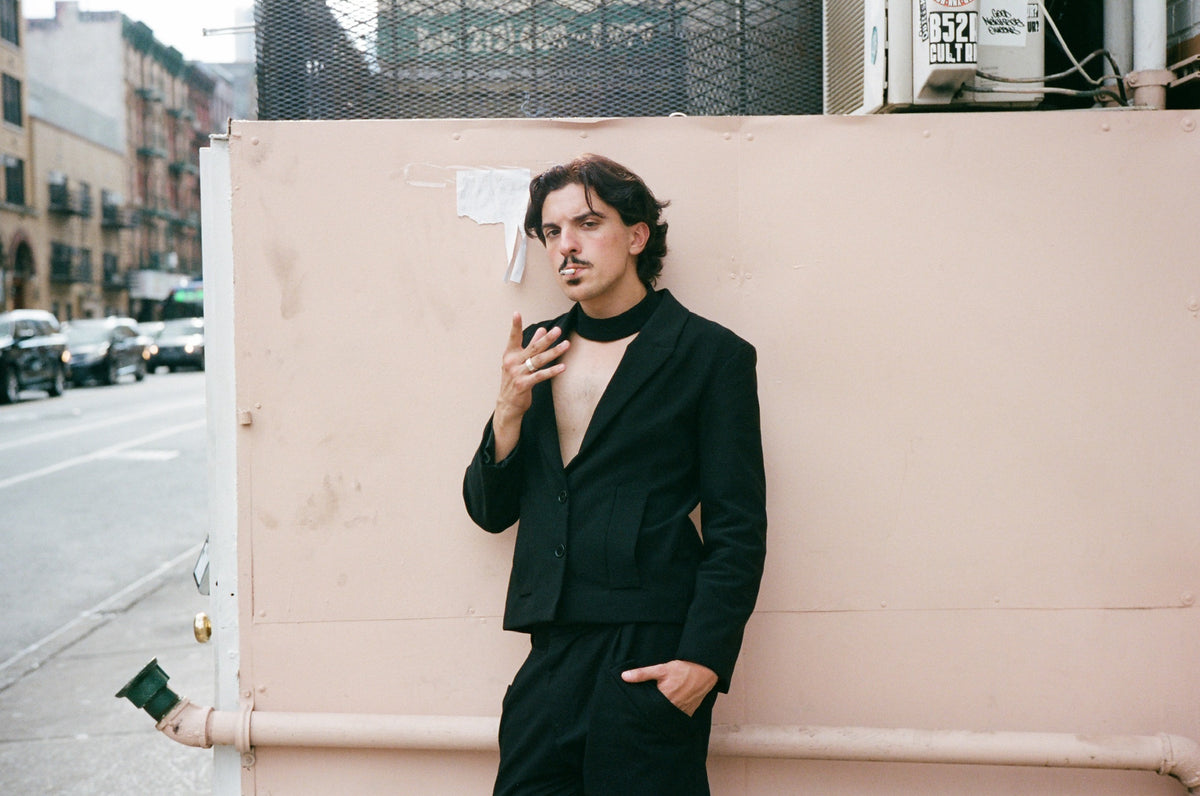 Figure smoking against a pink wall on a city street