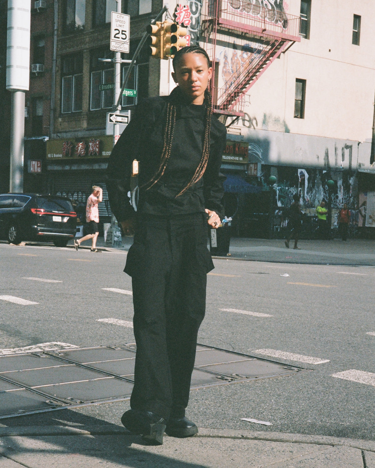 Figure in a black jacket standing on a sunlit street corner