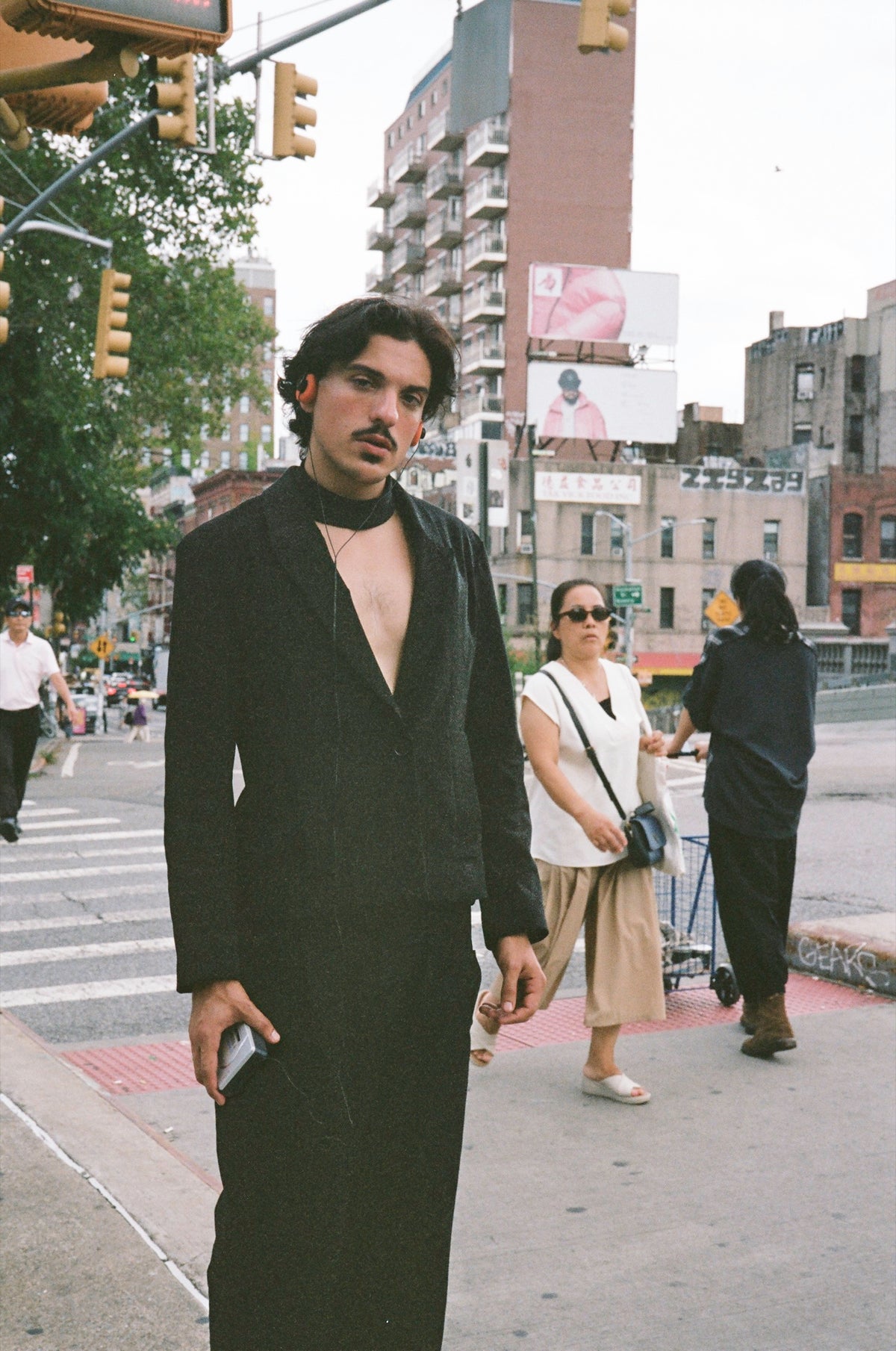Figure in a long black suit and choker standing on a busy street corner